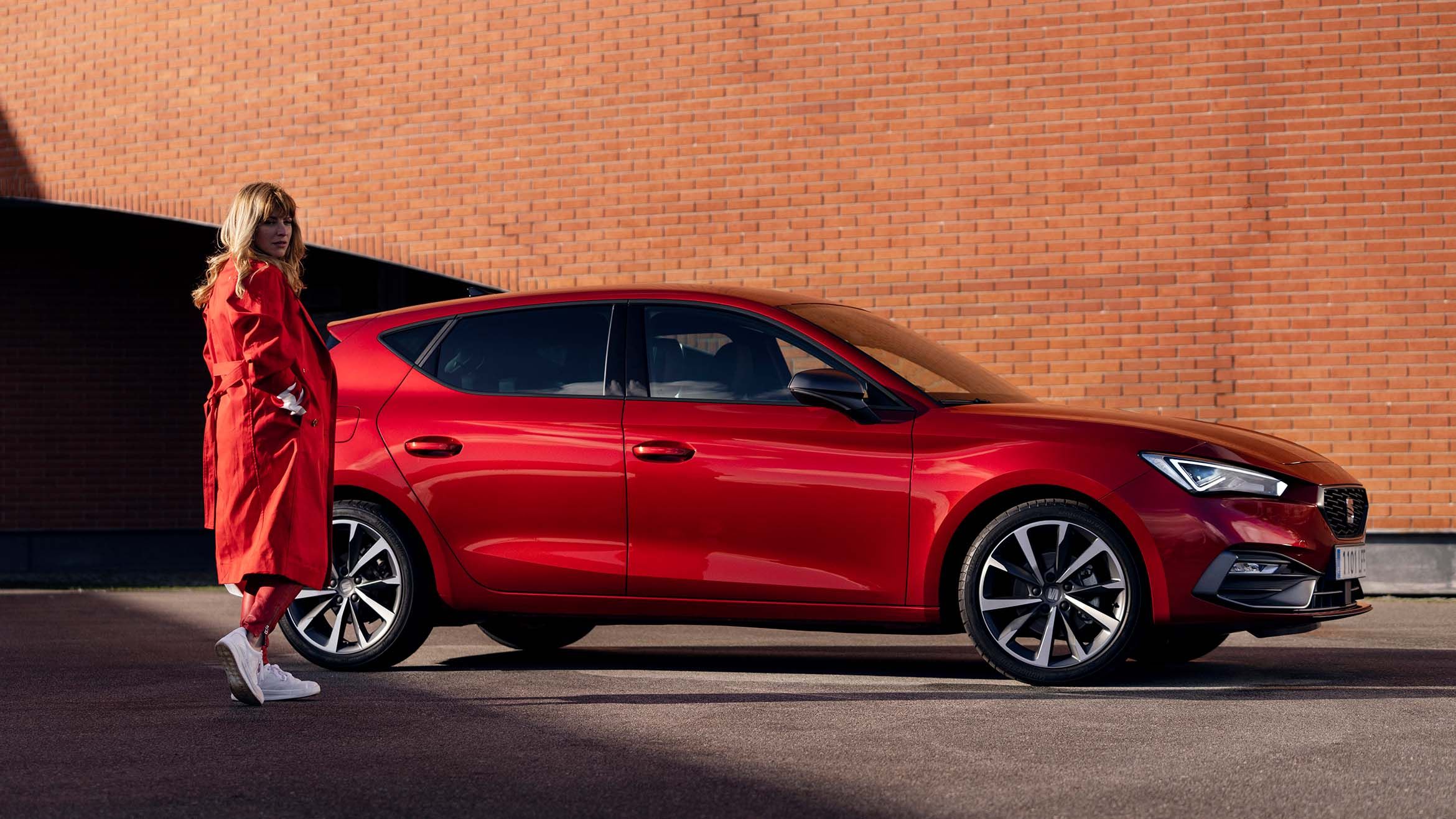 SEAT Leon mellett piros ruhás nő